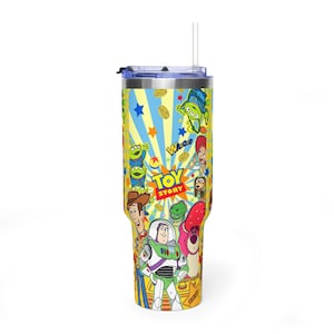 May include: A yellow and blue tumbler featuring characters from the Toy Story film. The tumbler has a straw and a lid. The design includes Woody, Buzz Lightyear, and the Little Green Men. The words "Toy Story" are also visible.