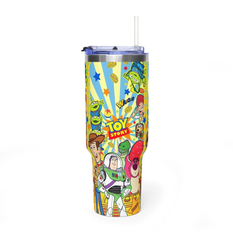 May include: A yellow and blue tumbler featuring characters from the Toy Story film. The tumbler has a straw and a lid. The design includes Woody, Buzz Lightyear, and the Little Green Men. The words "Toy Story" are also visible.