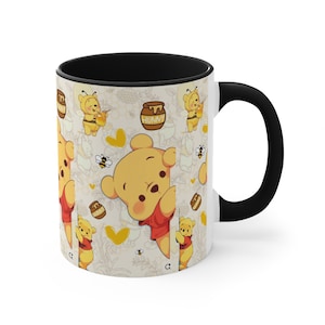 May include: A white ceramic mug with a black interior and handle. The mug features a repeating pattern of Winnie the Pooh, bees, and honey pots. The design is in yellow, red, and black.