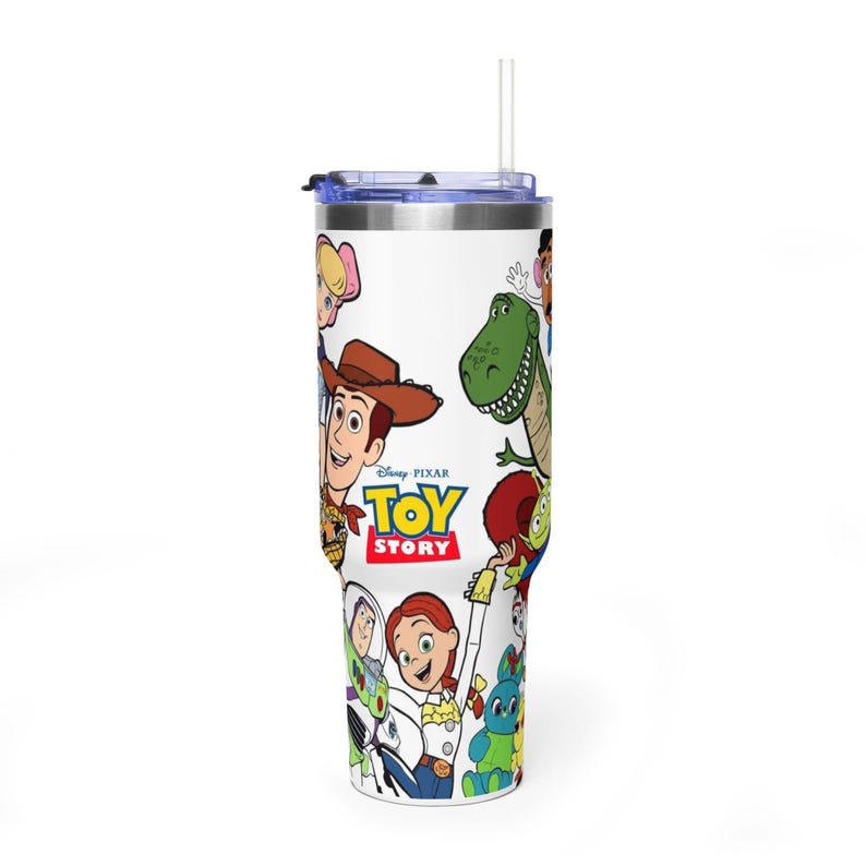 May include: A white tumbler featuring characters from the Disney Pixar movie Toy Story. The tumbler has a blue lid and a clear straw. The Toy Story logo is visible, along with images of Woody, Buzz Lightyear, and other characters.