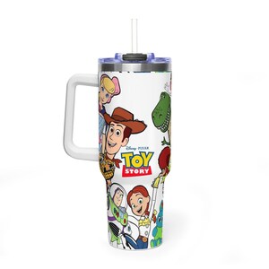 May include: White tumbler featuring characters from the Disney Pixar movie Toy Story. The tumbler has a white handle, a blue lid, and a white straw. The tumbler has a wrap-around design with images of Woody, Buzz Lightyear, and other characters.