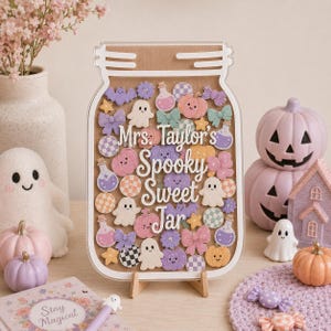 Puede incluir: Un letrero de acrílico transparente con forma de frasco y panel trasero de madera, lleno de iconos coloridos que incluyen fantasmas, calabazas, lazos, estrellas y pociones. El texto Mrs. Taylor's Spooky Sweet Jar está impreso en color blanco.
