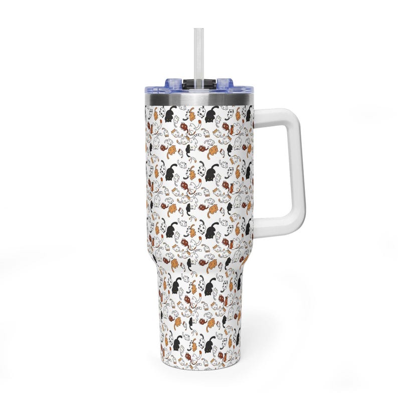 Op de afbeelding: Een witte beker met een handvat en een rietje, met een herhaald patroon van zwarte, bruine en oranje katten. De katten staan in verschillende poses tegen een achtergrond van witte wervelingen. Het deksel is blauw.