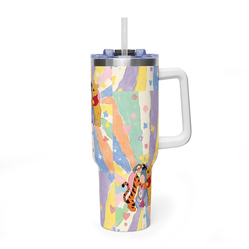 Puede incluir: Un vaso de acero inoxidable con asa y pajita transparente, que presenta un patr&oacute;n de rayos de sol en tonos pastel con ilustraciones de Winnie the Pooh, Tigger, Eeyore y Piglet, decorado con peque&ntilde;as flores y corazones rosas y azules.