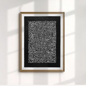 May include: Framed artwork featuring intricate white calligraphy on a black background. The gold frame surrounds the detailed script, creating a striking contrast. The artwork is displayed against a white wall, with natural light casting shadows.