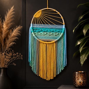 May include: A handcrafted wall hanging with a circular wooden frame. The design features a yellow sun, blue and green waves, and long, colorful yarn tassels in shades of yellow, blue, and green. It is a decorative piece for home decor.