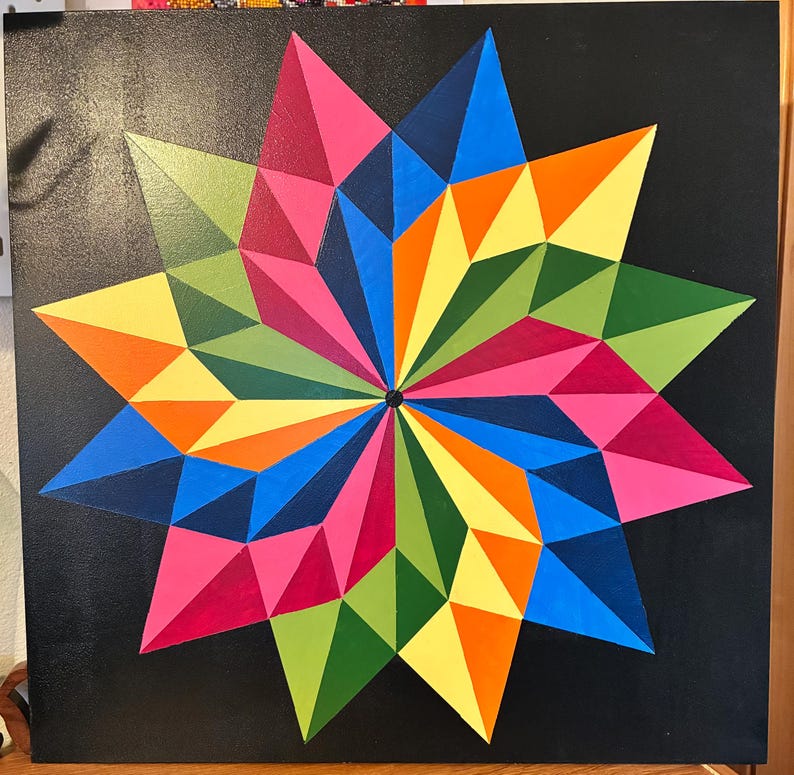 May include: A colorful geometric starburst painting on a black background. The artwork features a symmetrical design with triangular shapes in various colors, including pink, blue, orange, yellow, and green. The starburst radiates from a central black point.