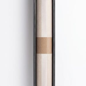 May include: A rectangular black box with a gold-colored decorative top. Inside, a rolled-up item is visible, wrapped with a brown band. The item appears to be made of paper or a similar material. The background is plain white.