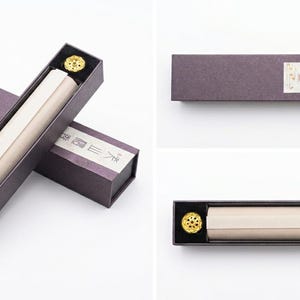 May include: A set of incense sticks in a rectangular box. The box is dark purple with a light beige scroll inside. A gold-colored incense holder is in the box. The box has Japanese text on the label.