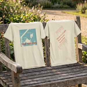 May include: A cream-colored t-shirt featuring a blue-toned graphic of a person singing into a microphone with the text THE SMITHS on the front, and the text There Is A Light That Never Goes Out printed in red on the back with surrounding lyrics.