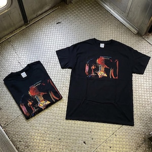 May include: Two black t-shirts with a colorful graphic design. The design features a red figure with other abstract shapes and the text "Lost Orchestra". The shirts are displayed on a metal surface.