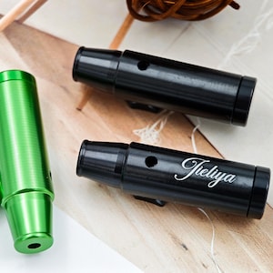May include: A selection of metal smoking pipes in black and green. One green pipe stands vertically, while two black pipes are horizontal. One black pipe features the word "Tieliya" in white script.