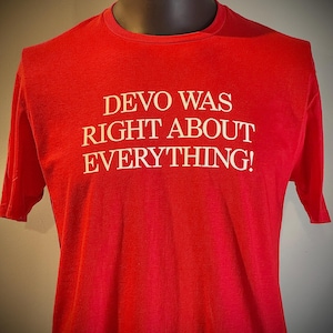 May include: A red t-shirt with the white text "DEVO WAS RIGHT ABOUT EVERYTHING!". The shirt is displayed on a mannequin. The t-shirt has short sleeves and a crew neck.