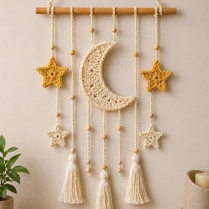 May include: A handcrafted wall hanging featuring a crocheted crescent moon and stars in shades of cream and yellow. Wooden beads and tassels add texture. The piece is suspended from a wooden dowel, creating a whimsical, bohemian-style nursery or home decor item.