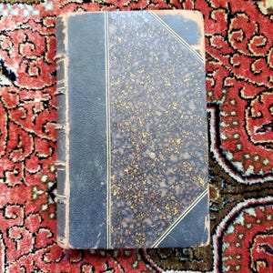 May include: A vintage hardcover book with a dark blue cover and gold accents. The cover has a marbled pattern with gold flecks.