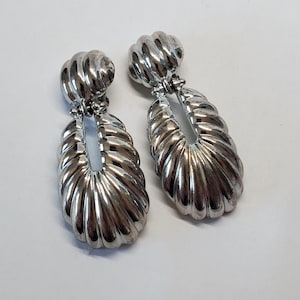 Può includere: Un paio di orecchini pendenti in argento con un design attorcigliato. Gli orecchini sono di forma ovale con un ritaglio al centro.