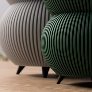 May include: Two decorative, modern accent tables. One is a light gray color, and the other is dark green. Both have a rounded shape with vertical grooves and black legs. The tables are on a light brown wooden floor.