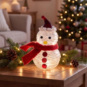 Puede incluir: Una figura de muñeco de nieve de vidrio transparente con superficie texturizada, que presenta un sombrero de vidrio rojo con borde blanco, una bufanda de punto roja brillante, dos ojos negros, una nariz amarilla y tres botones rojos, iluminada desde el interior.