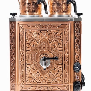 Può includere: Una teiera color rame con due teiere sulla parte superiore. Il pannello frontale presenta un ornato disegno floreale. Ha un rubinetto, un indicatore di temperatura e manopole. Le teiere hanno manici e coperchi neri.