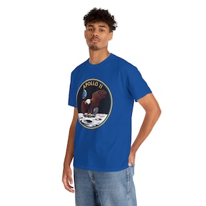May include: Royal blue t-shirt featuring a circular graphic of an eagle landing on the moon, with the text "APOLLO 11" in a gold border. The eagle has brown and white feathers. The shirt is made of a soft material.