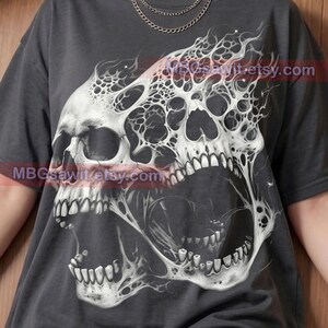 May include: A charcoal gray t-shirt featuring a large, detailed white graphic of two conjoined, screaming skulls with a web-like, distorted texture. The shirt includes the text "Pepper Comfort Colors" at the bottom and "MBGsawit.etsy.com" overlaid.