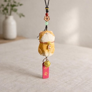 May include: A wooden cat figurine with a red and gold bell and a red tag with Chinese characters. The cat is orange and white with a red collar and a small gold charm. The figurine hangs from a black cord with decorative beads.
