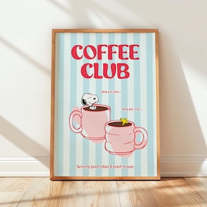 May include: A framed print with a light blue and white striped background. The words "COFFEE CLUB" are in red, above two pink coffee mugs. Snoopy is in one mug. Text reads "serving good vibes & fresh brews."