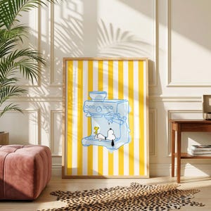 May include: A framed wall art print featuring a light blue line drawing of an espresso machine on a background of vertical yellow and white stripes. The illustration depicts the cartoon character Snoopy and Woodstock inside the machine.