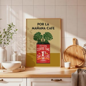 May include: A framed art print with a coffee theme. The print features a red coffee pot illustration with the words "Rise n Shine Coffee Time Camp Life Morning Adventure Awaits." The top of the print reads "Por La Mañana Cafe."
