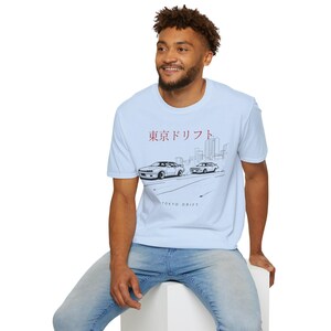 May include: Light blue t-shirt featuring a graphic of two cars drifting, with the text "TOKYO DRIFT" and Japanese characters. The design is in black and white, with a cityscape silhouette in the background.