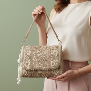 May include: A beige clutch bag with detailed beadwork and a flap. It has a beaded strap and a pearl tassel. The design incorporates floral and geometric patterns, making it a sophisticated accessory for any occasion.