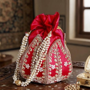 May include: A vibrant red drawstring pouch bag featuring intricate gold-toned leaf-shaped embroidery and small white bead accents. The bag includes a long, multi-strand white pearl-like beaded handle that drapes elegantly over the front surface.