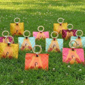 Peut inclure: Plusieurs sacs à main colorés à motifs, avec des poignées en anneau dorées. Les sacs présentent une image centrale d'une femme en robe jaune. Les sacs sont de différentes couleurs, dont le jaune, le rose, l'orange et le bleu.