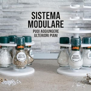 Può includere: Portaspezie modulare bianco con barattoli di vetro pieni di grani di pepe e sale. I barattoli hanno coperchi verdi ed etichette. Il testo "SISTEMA MODULARE" è visualizzato sopra il portaspezie.