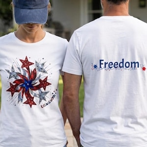 Puede incluir: Dos personas vistiendo camisetas blancas con diseños patrióticos. Una camiseta presenta un diseño de explosión de estrellas con estrellas rojas, blancas y azules, y el texto "USA 250th". La otra camiseta muestra la palabra "Freedom" en azul.