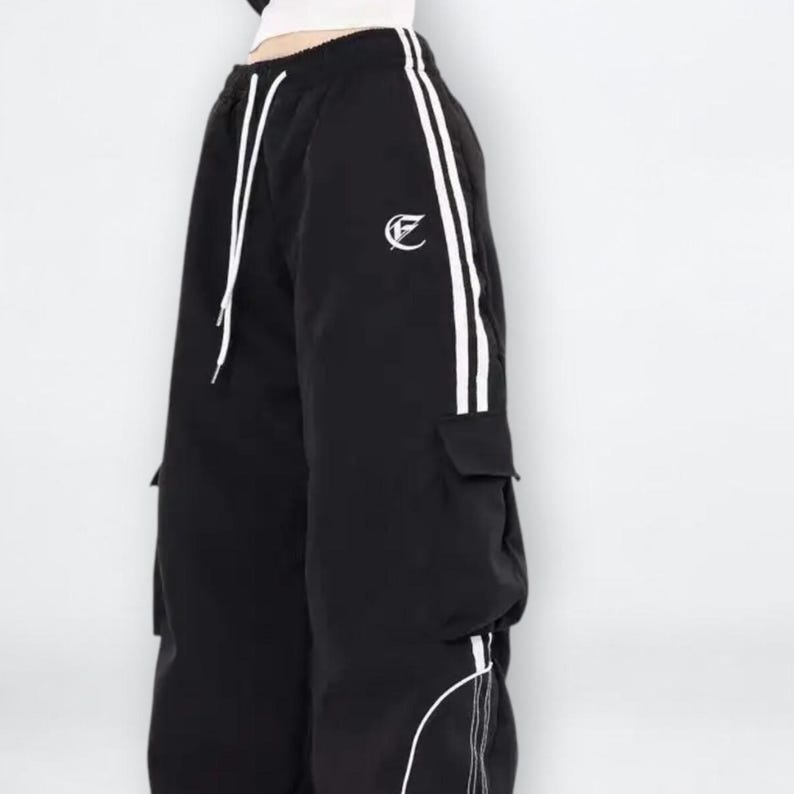 Baggy Cargo Pants | Casual Wide Leg Joggers | Modern Y2K Streetwear 

Woman wearing black baggy cargo pants with wide leg fit and side stripe detail styled for Y2K streetwear fashion.