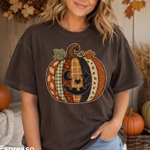 May include: A dark brown short-sleeve t-shirt featuring a large, central graphic of a pumpkin made of various patchwork-style fabric patterns in shades of orange, green, and tan, with a carved face showing a crescent moon, heart, and star.