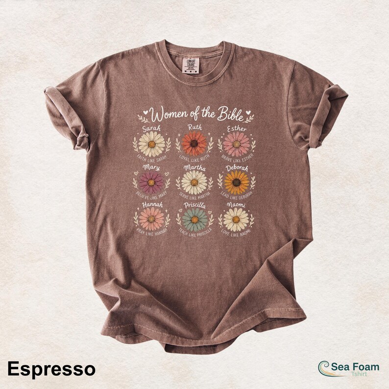 May include: Espresso-colored t-shirt featuring the text "Women of the Bible" above nine daisy illustrations, each with a woman's name and a related phrase. The shirt also has the Sea Foam T-shirt logo.