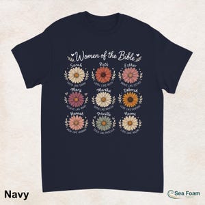 May include: Navy blue t-shirt featuring the text "Women of the Bible" above nine daisy flower designs. Each flower has a name and a related phrase. The shirt is a comfortable, casual wear item.