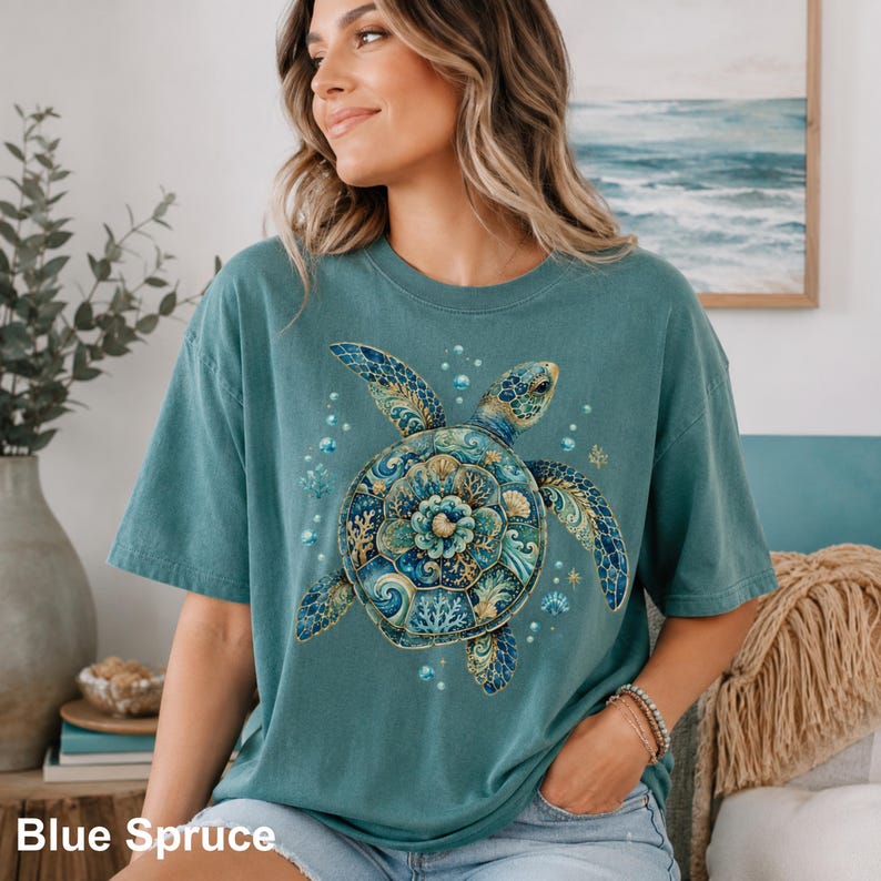 Puede incluir: Una camiseta de manga corta color verde azulado con un gr&aacute;fico grande de una tortuga marina en la parte delantera. El caparaz&oacute;n de la tortuga est&aacute; decorado con intrincados patrones azules, dorados y verdes, rodeado de burbujas y corales.