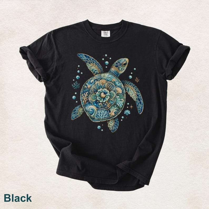 Puede incluir: Una camiseta negra con un gr&aacute;fico central de una tortuga marina con un caparaz&oacute;n compuesto por intrincados patrones florales y de coral en tonos azul, verde azulado y dorado. El dise&ntilde;o incluye peque&ntilde;as burbujas, estrellas de mar y conchas.