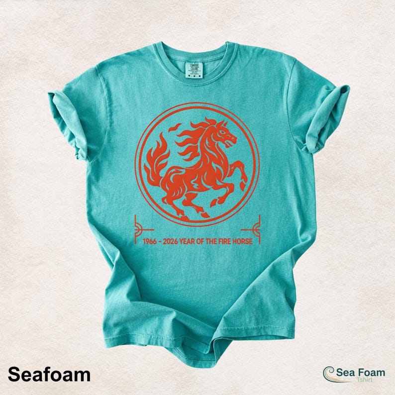 May include: A seafoam green short-sleeve t-shirt featuring a circular orange graphic of a rearing horse. Below the circle, the text reads 1966 - 2026 YEAR OF THE FIRE HORSE. The shirt has a crew neckline and a standard fit with a folded sleeve detail.