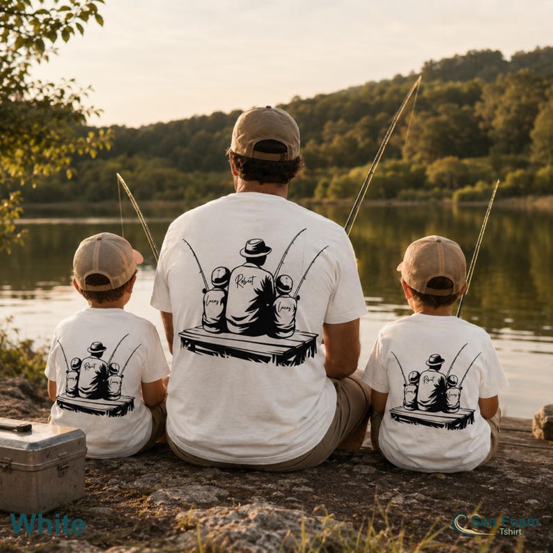 May include: White t-shirts with a black graphic of a person fishing with two children. The graphic includes the text "Robert" and "Lucas" and "James". The shirts are worn by a person and two children fishing by a lake.