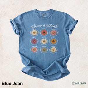 May include: Blue jean t-shirt featuring the text "Women of the Bible" with floral designs and names like Sarah, Ruth, and Esther. The shirt has a crew neck and short sleeves, made of soft material.