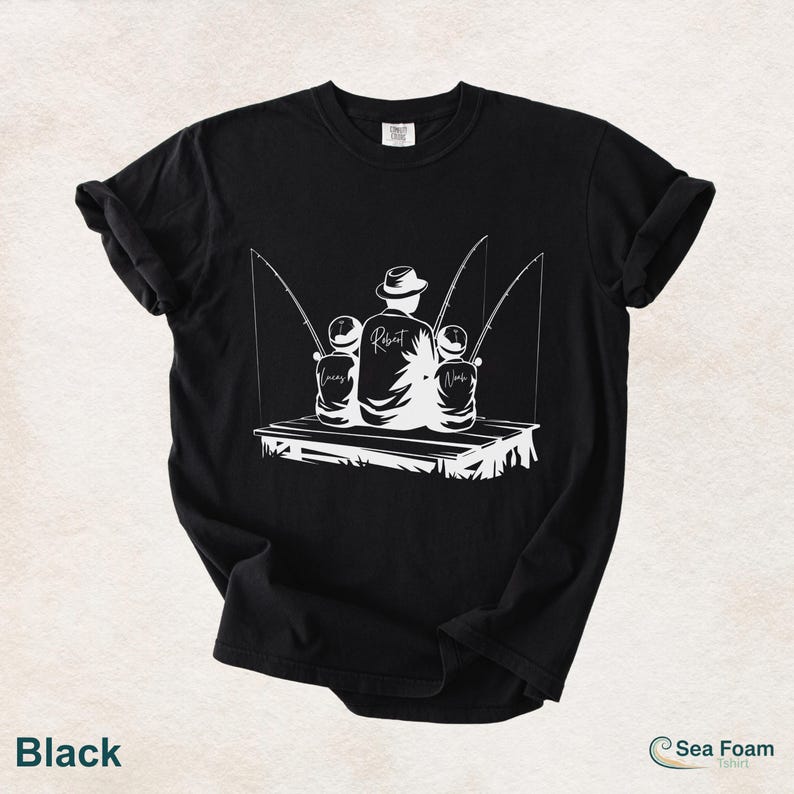 May include: Black t-shirt with a white graphic of a father and two children fishing on a dock. The father's back is turned, and the children's names, Lucas and Noah, are printed on the shirt. The word "Robert" is printed on the father's back.