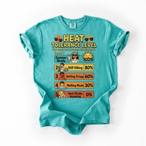 May include: Turquoise t-shirt with a graphic illustrating a "Heat Tolerance Level" with summer-themed icons and text. The design includes levels from "Summer Ready" to "Heat Stroke Incoming", with corresponding percentages.