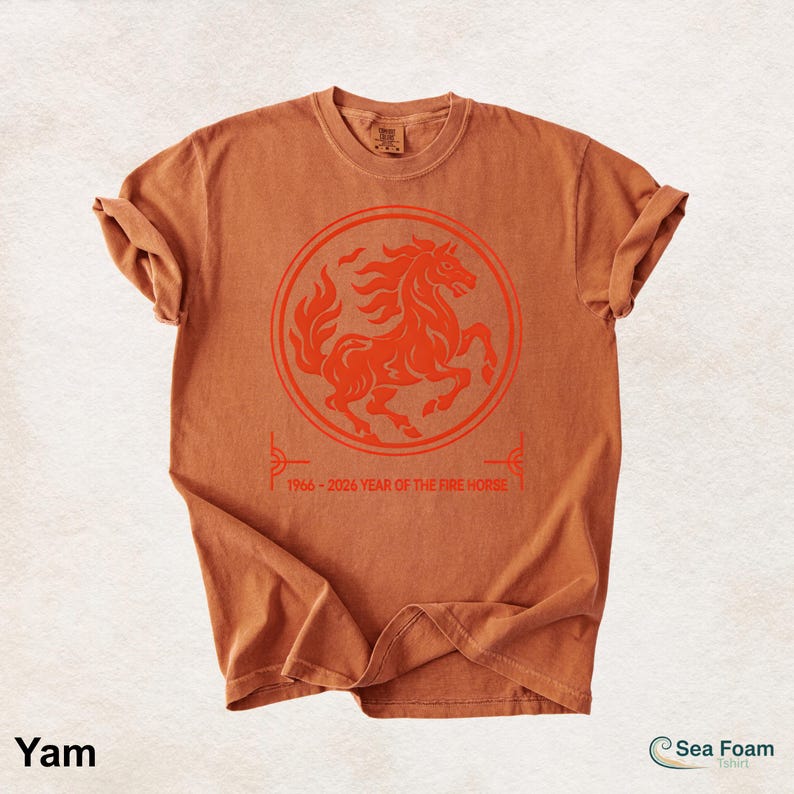 May include: A rust-colored short-sleeve t-shirt featuring a circular graphic of a rearing horse in a darker orange tone. Below the circle, the text reads 1966 - 2026 YEAR OF THE FIRE HORSE. The shirt has a crew neckline and a relaxed fit.