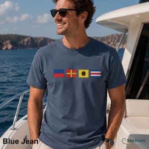 May include: A blue jean t-shirt with nautical flag graphics. The shirt features a series of colorful flags in red, yellow, blue, and white. The text "Blue Jean" is at the bottom left of the image.