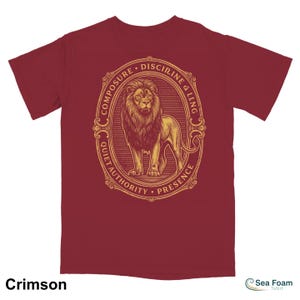 May include: Crimson t-shirt featuring a detailed illustration of a lion inside an oval frame. The frame includes the words "Composure, Discipline, Quiet Authority, Presence." The shirt is a solid crimson color.