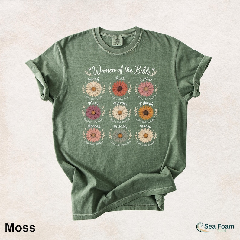 May include: Moss green t-shirt featuring the text "Women of the Bible" above nine daisy illustrations, each with a woman's name and a related phrase. The shirt has rolled-up sleeves and a crew neck.